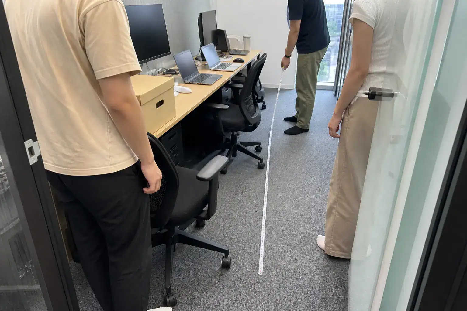 三名工作者用捲尺測量台南微型辦公室椅背與走道空間